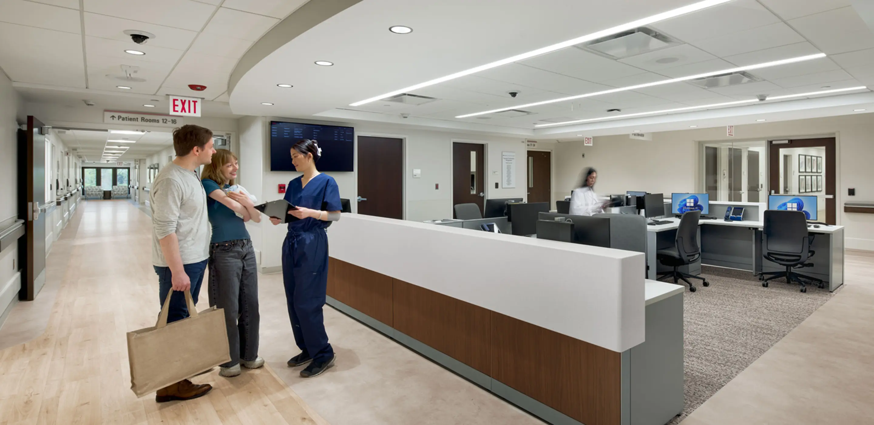 Family consulting with nurse at hospital reception desk. Modern healthcare setting with computers and clear signage.