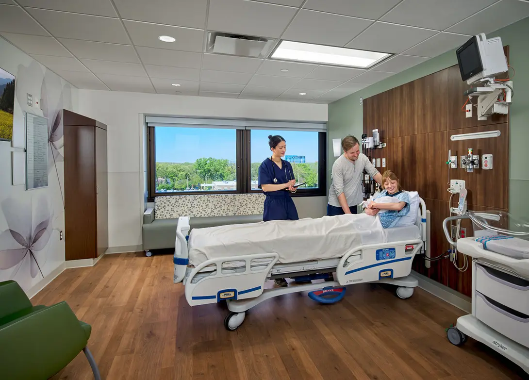 Hospital delivery room with nurse, new parents, and newborn baby in hospital bed.