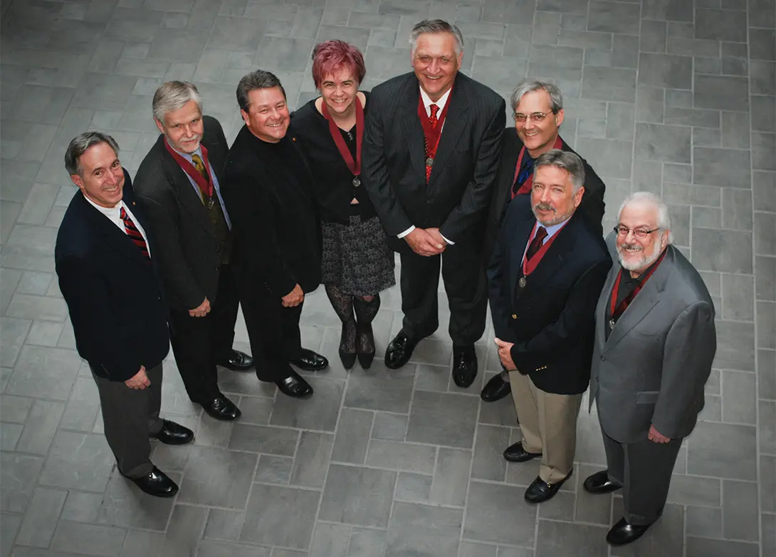 Group of eight professionals in formal attire standing together, smiling up at the camera.