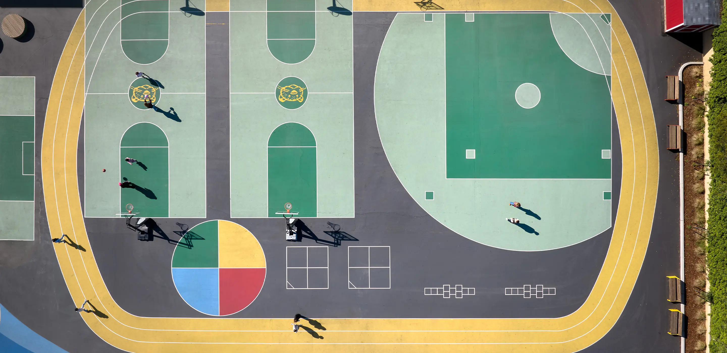 Aerial view of colorful sports courts and running track in a park with people playing basketball.