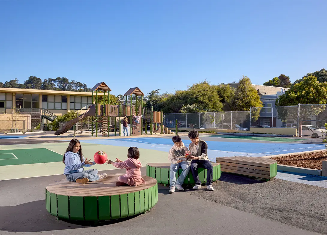 Children playing with a ball and sitting near a playground on a sunny day.