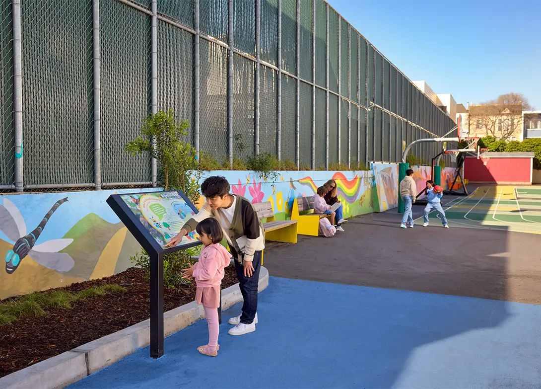 Children learning and playing in a colorful outdoor playground with educational signs and murals.