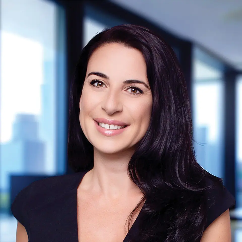 Smiling professional woman in an office setting with large windows in the background.