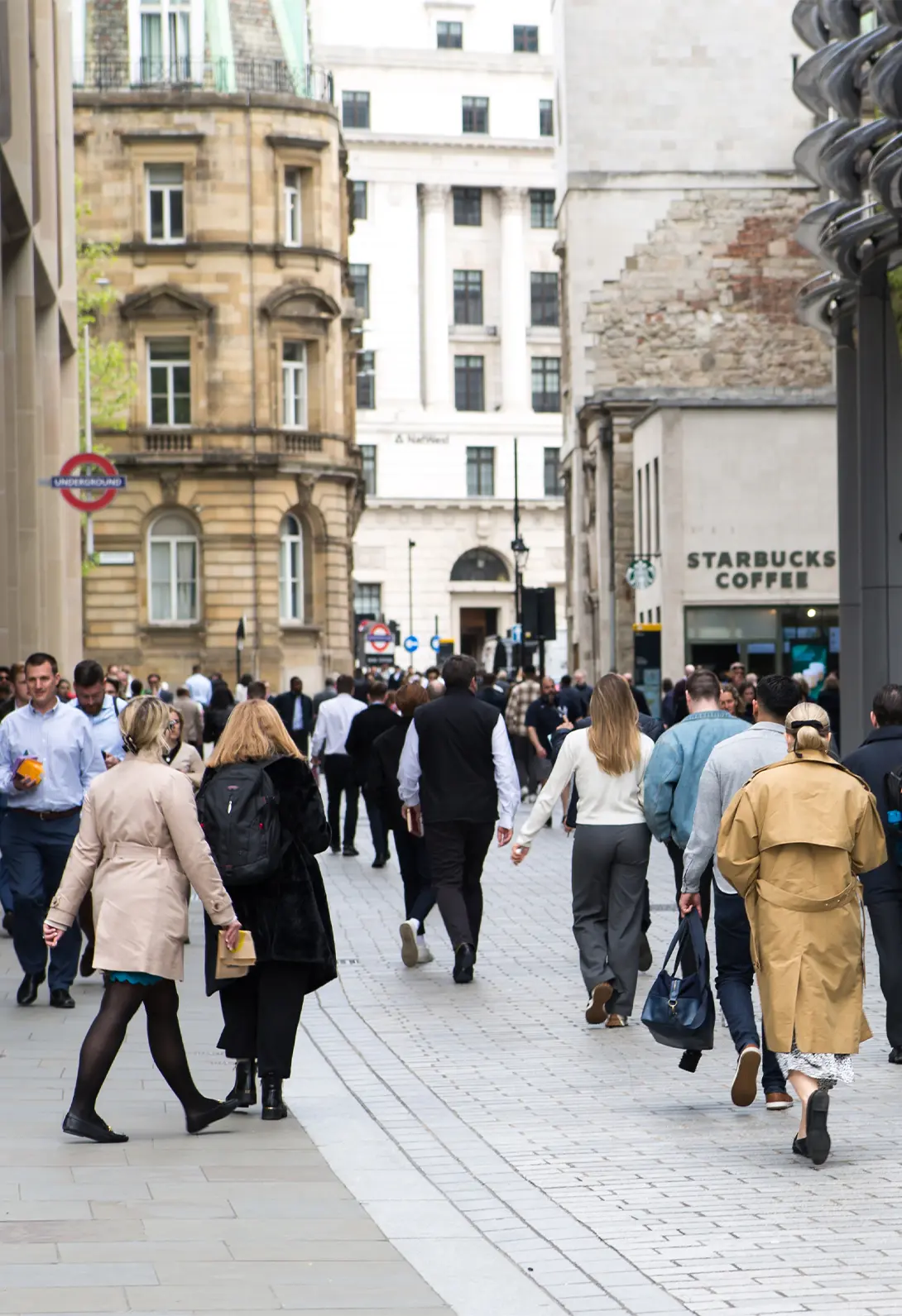 Busy London street with people walking near historical buildings and Starbucks, close to Underground station.