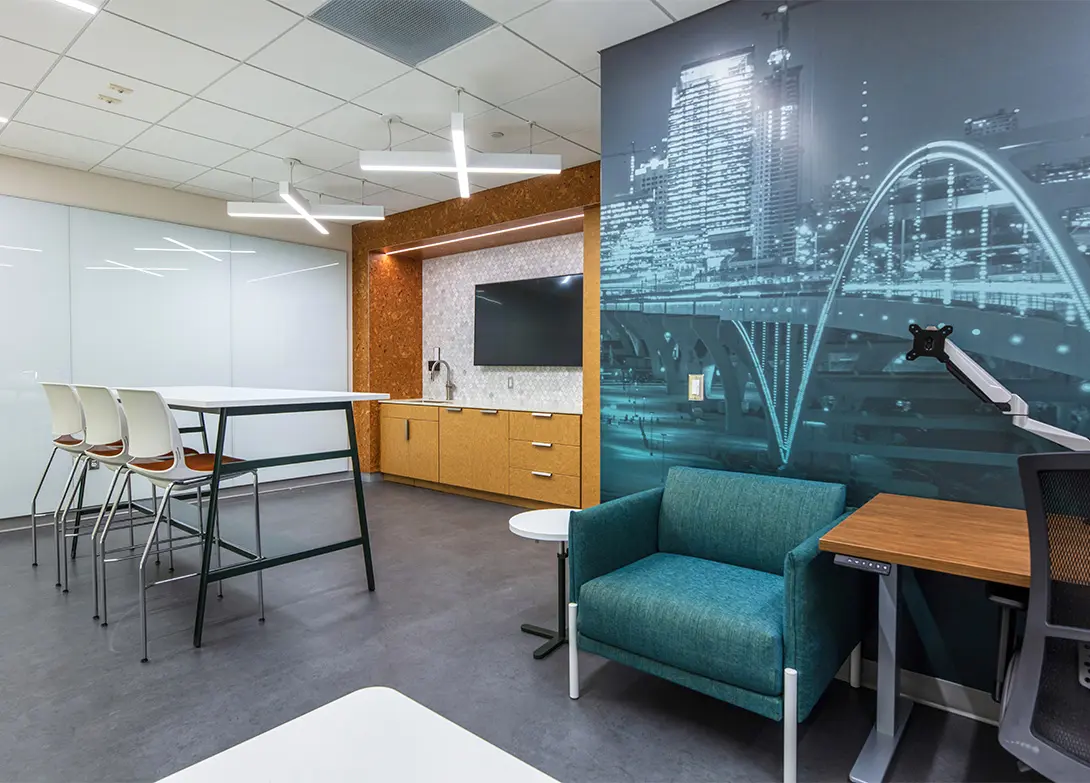 Modern office lounge with high table, chairs, and wall art featuring a cityscape.