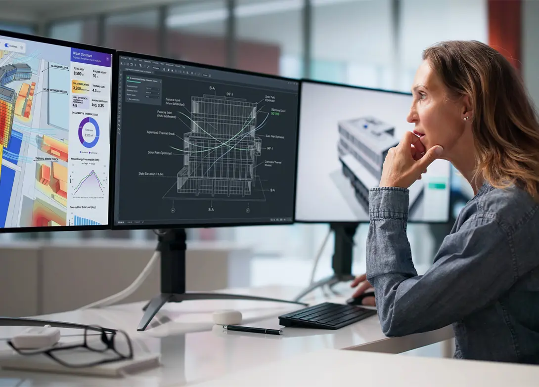 Architect analyzing building design on multiple computer monitors in modern workspace.