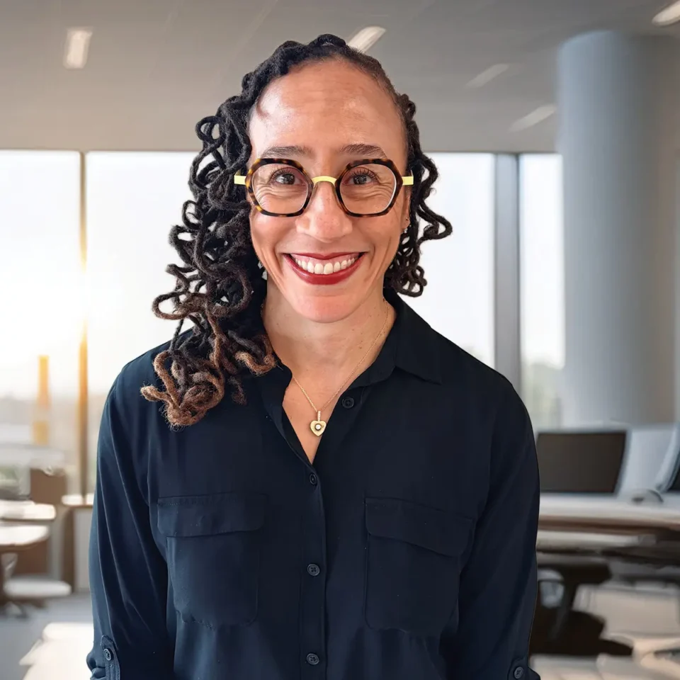 Smiling person with glasses and dreadlocks in a modern office setting.