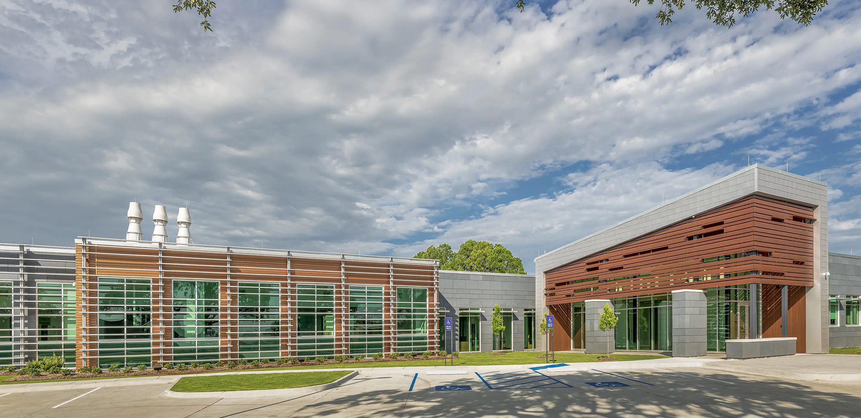 Modern building exterior with large windows and wooden accents, under a partly cloudy sky.