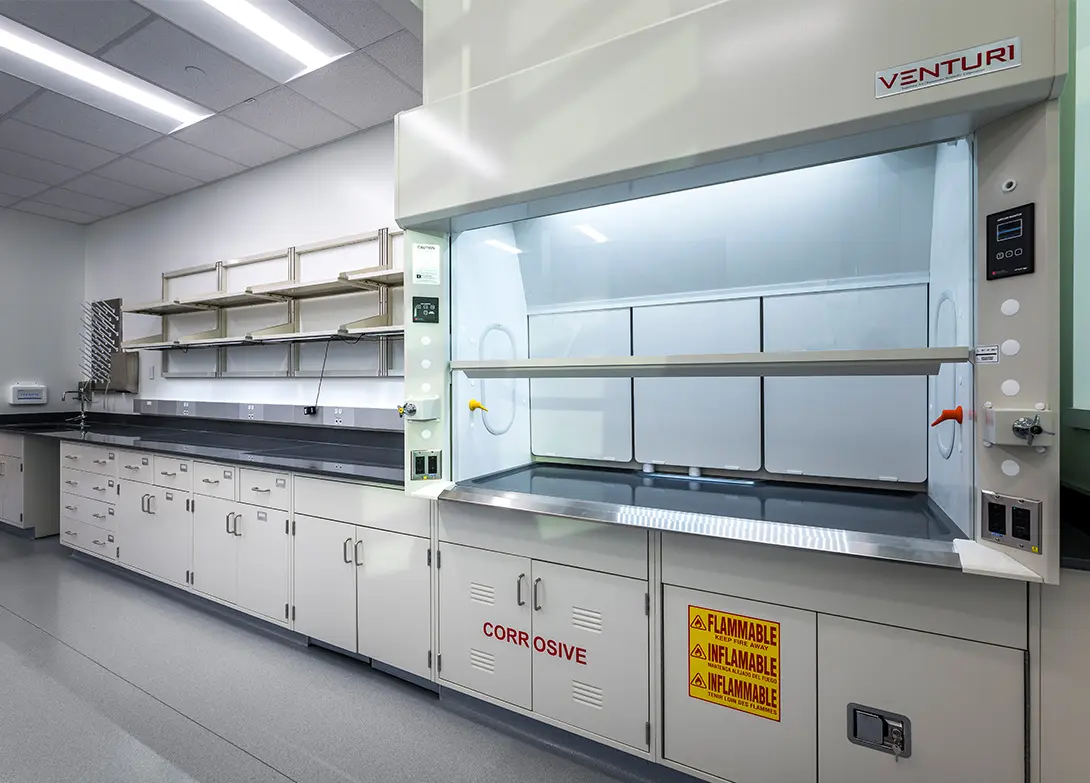 Modern laboratory with fume hood, safety signs, and storage cabinets for chemical research and development.