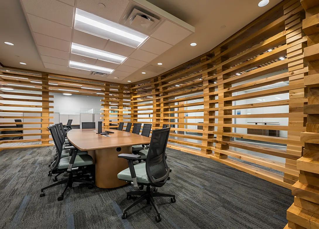 Modern conference room with wooden slat walls and black office chairs around a large table.