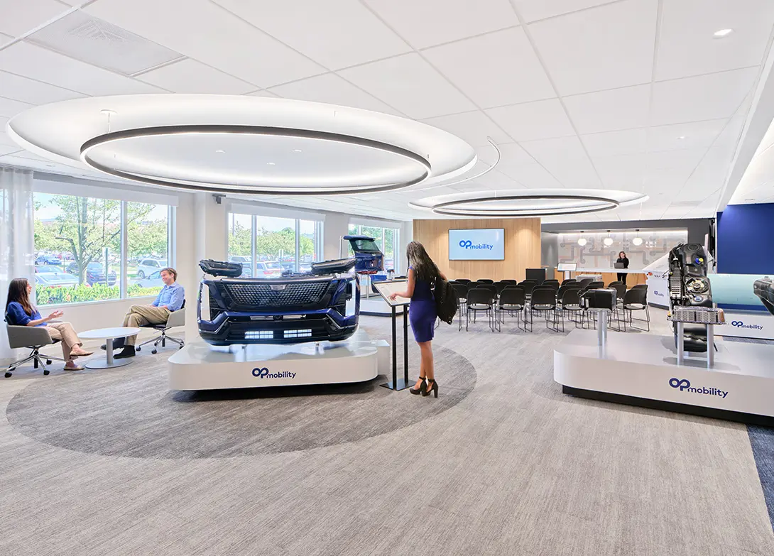 Modern automotive showroom with interactive displays, people engaging, and Op Mobility branding.