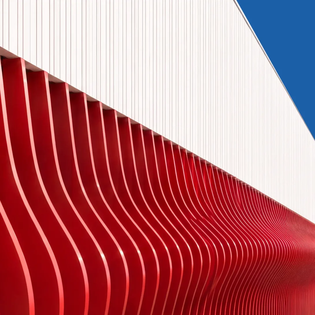 Modern building facade with wavy red panels and white upper section against blue sky, showcasing architectural design.