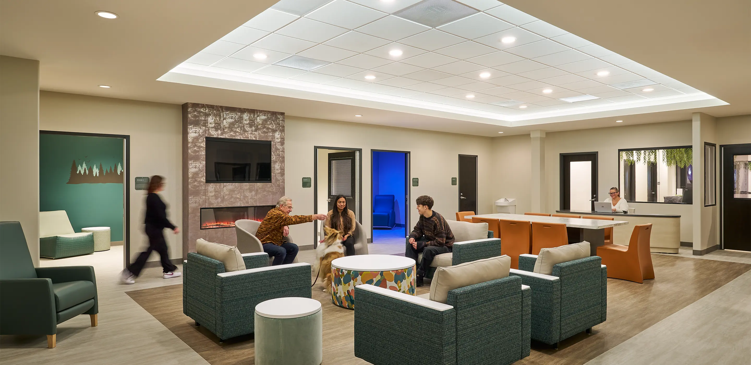Modern waiting area with comfortable seating, people relaxing, and staff at reception desk in a well-lit space.