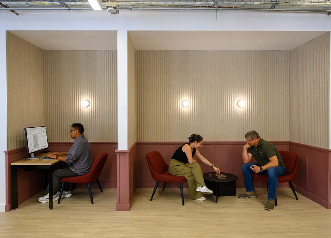 Modern office space with collaborative meeting areas and private workspace, featuring stylish maroon chairs.