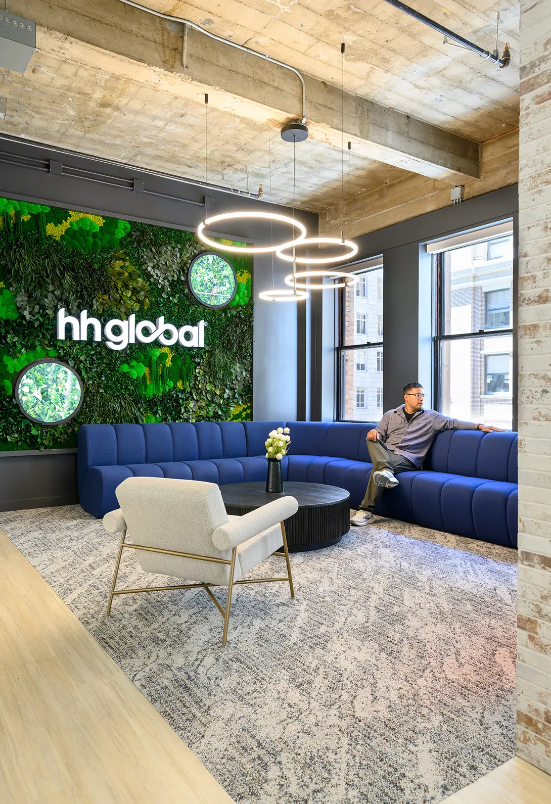 Modern office lounge with green wall, circular lights, and blue sectional sofa at hhglobal.