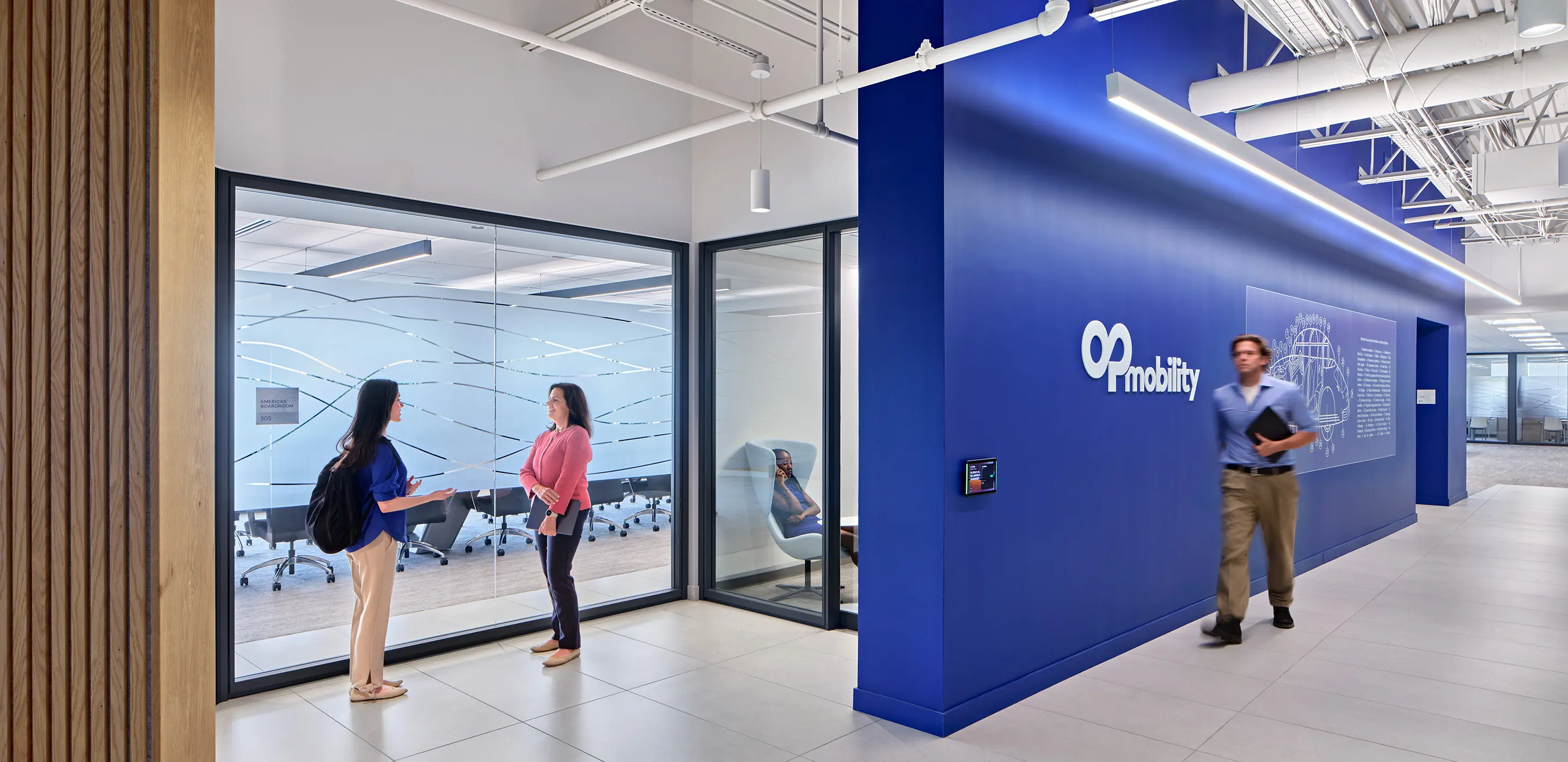 Office hallway with mobility sign, people conversing, and a man walking, modern workspace interior design.