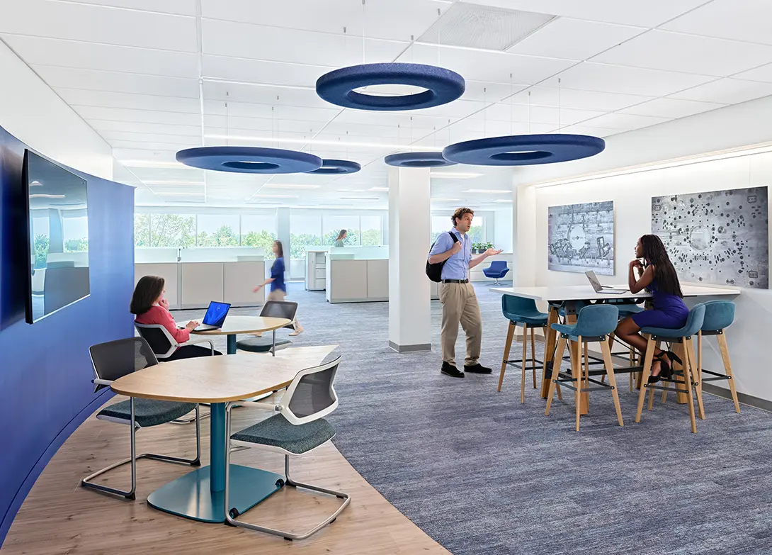 Modern open office space with employees collaborating and working on laptops, featuring blue decor and natural light.